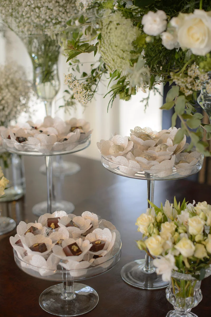 Mesa de casamento com doces finos em bandejas de vidro e flores brancas