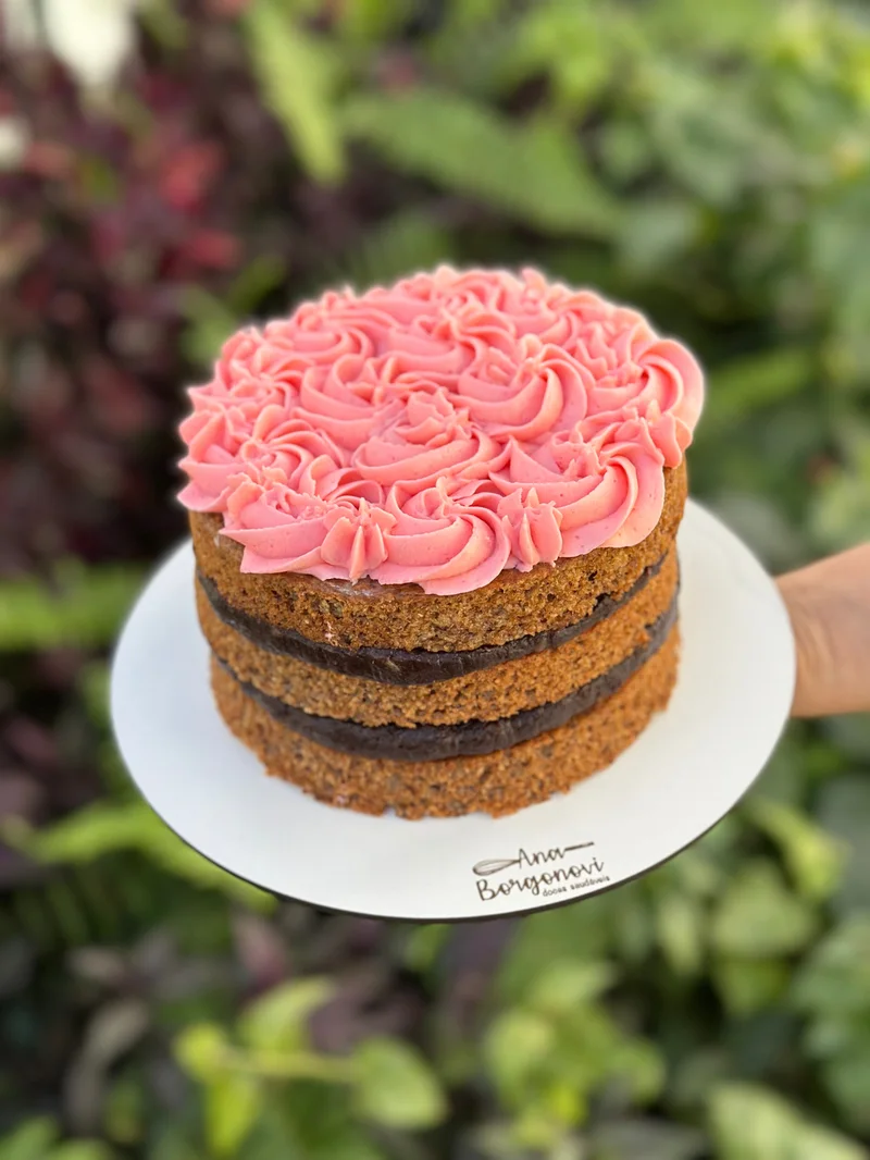 Bolo infantil com cobertura rosa em rosetas, segurado sobre jardim